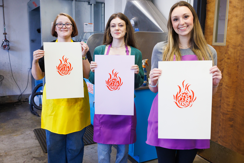 Three female students stand in a line holding posters that they printed that say Spot Fire Press.