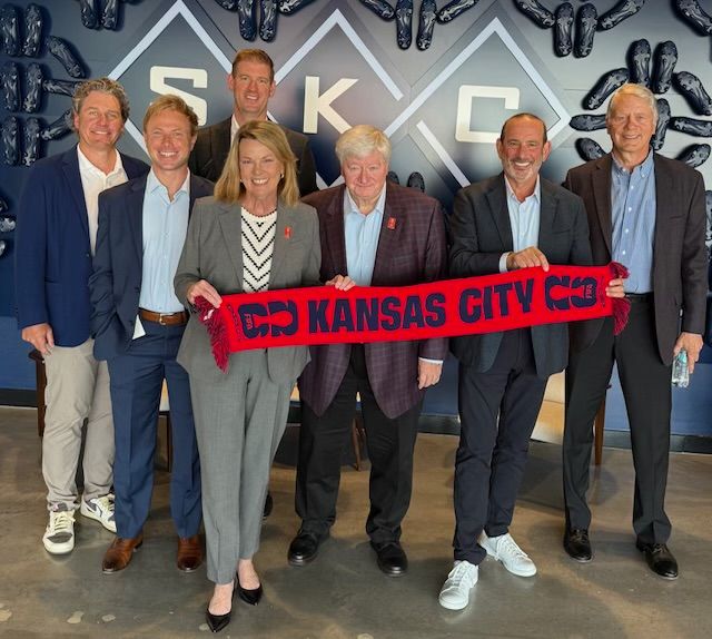 A group of people in professional attire hold a red banner that says Kansas City.
