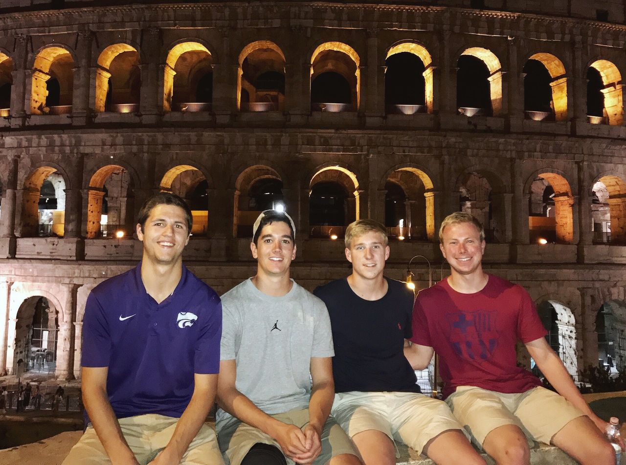 Four students are seated in front of the Coliseum at night.