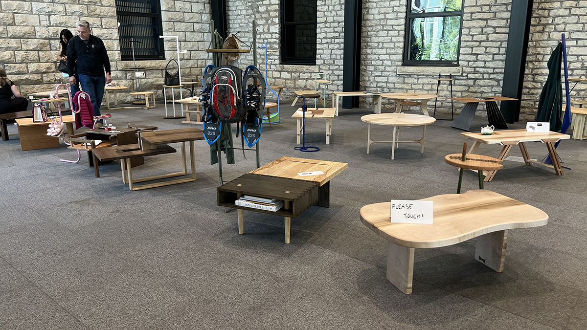 Several pieces of unique, student-design wooden furniture sit on a floor as part of a showcase.