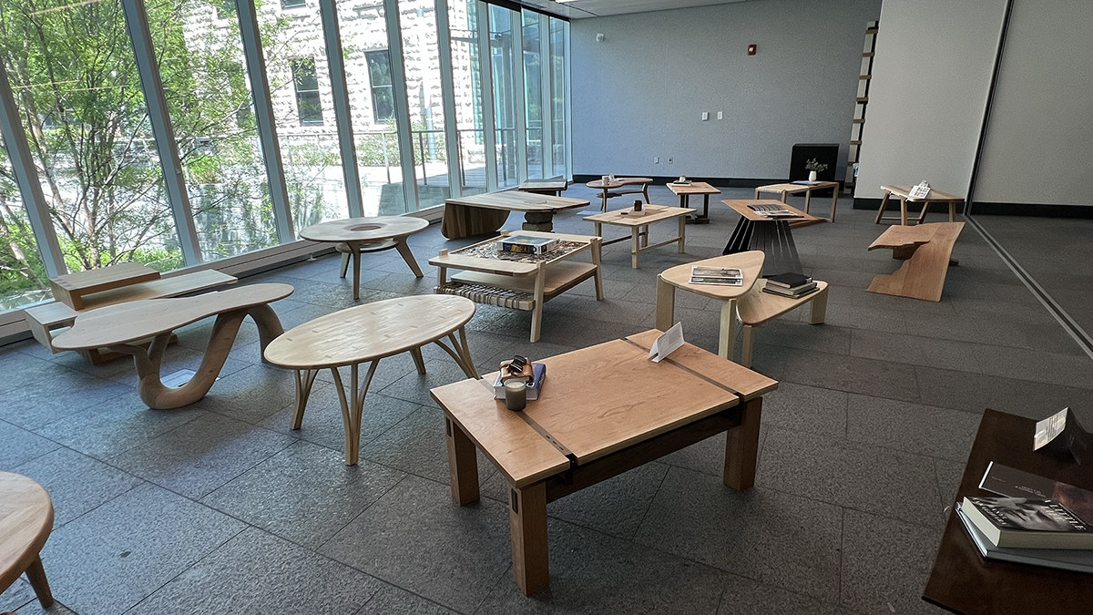 Several pieces of wooden furniture sit on display next to a wall of windows.
