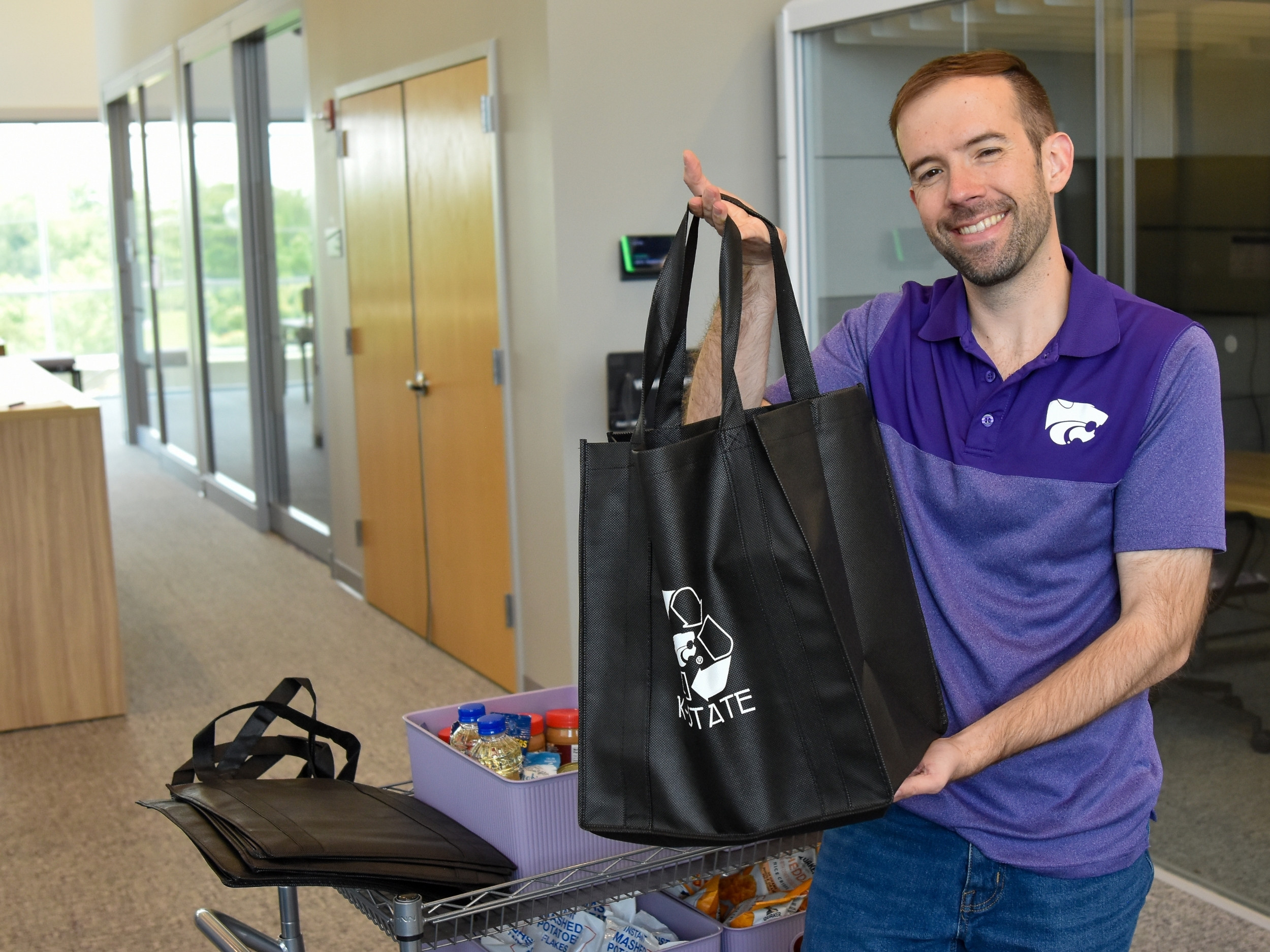 Steven Brockschmidt stands next to the Cats' Cupboard Cart, holding a black reusable grocery bag