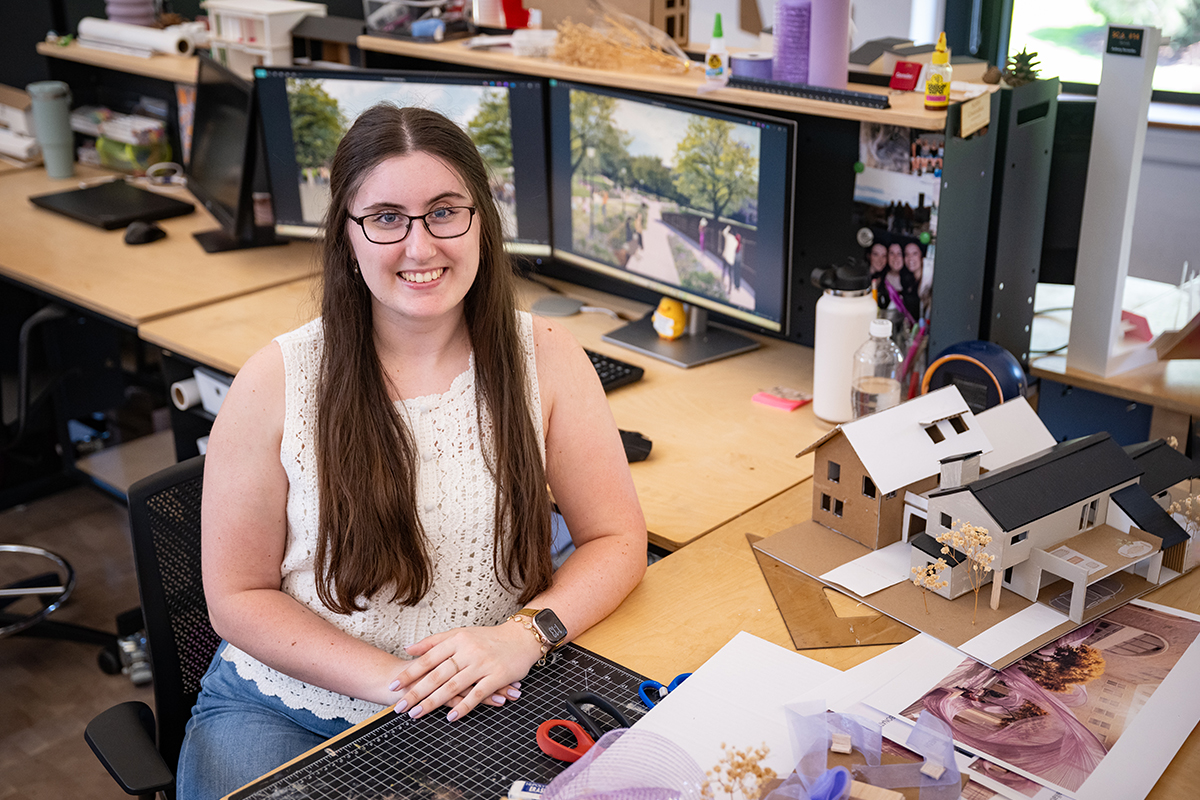 A female architecture graduate student sits at her desk and poses for a portrait.