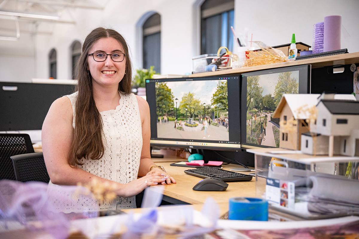 A female architecture graduate students sits at her work studio and poses for a portrait.