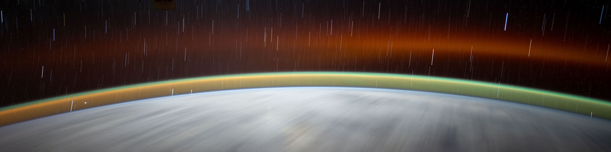 A satellite view shows the bright blue orb of earth with swirling white clouds over it and a green ring of haze as well.