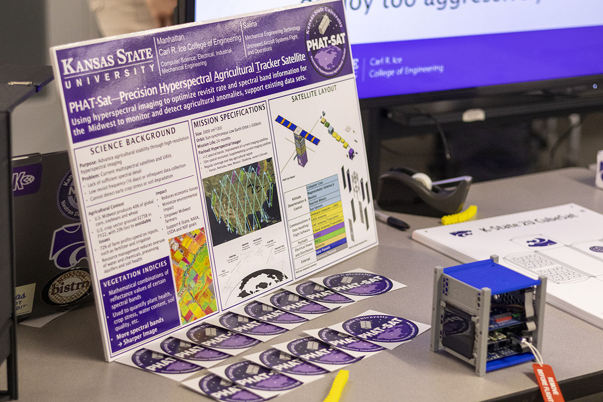A poster on a table shows information about PHAT-Sat, a student-designed and led mission to launch a satellite to monitor crops on Earth using hyperspectral cameras.