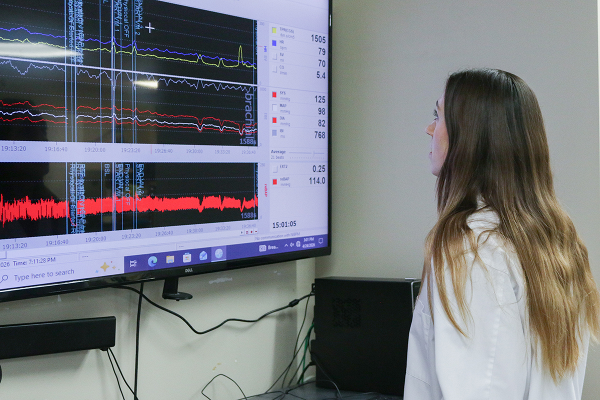 A graduate student in a white labcoat looks at various heart wave signals on a monitor.