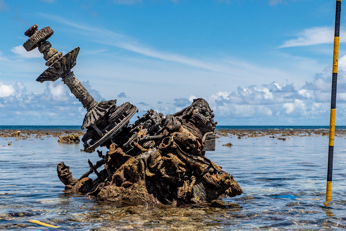 An old, rusted airplane engine sticks out a shallow ocean beach.