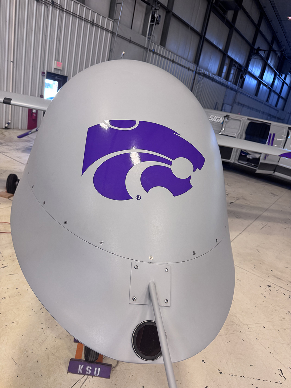 A close-up view of the nose of a gray uncrewed aircraft with a purple powercat on it.
