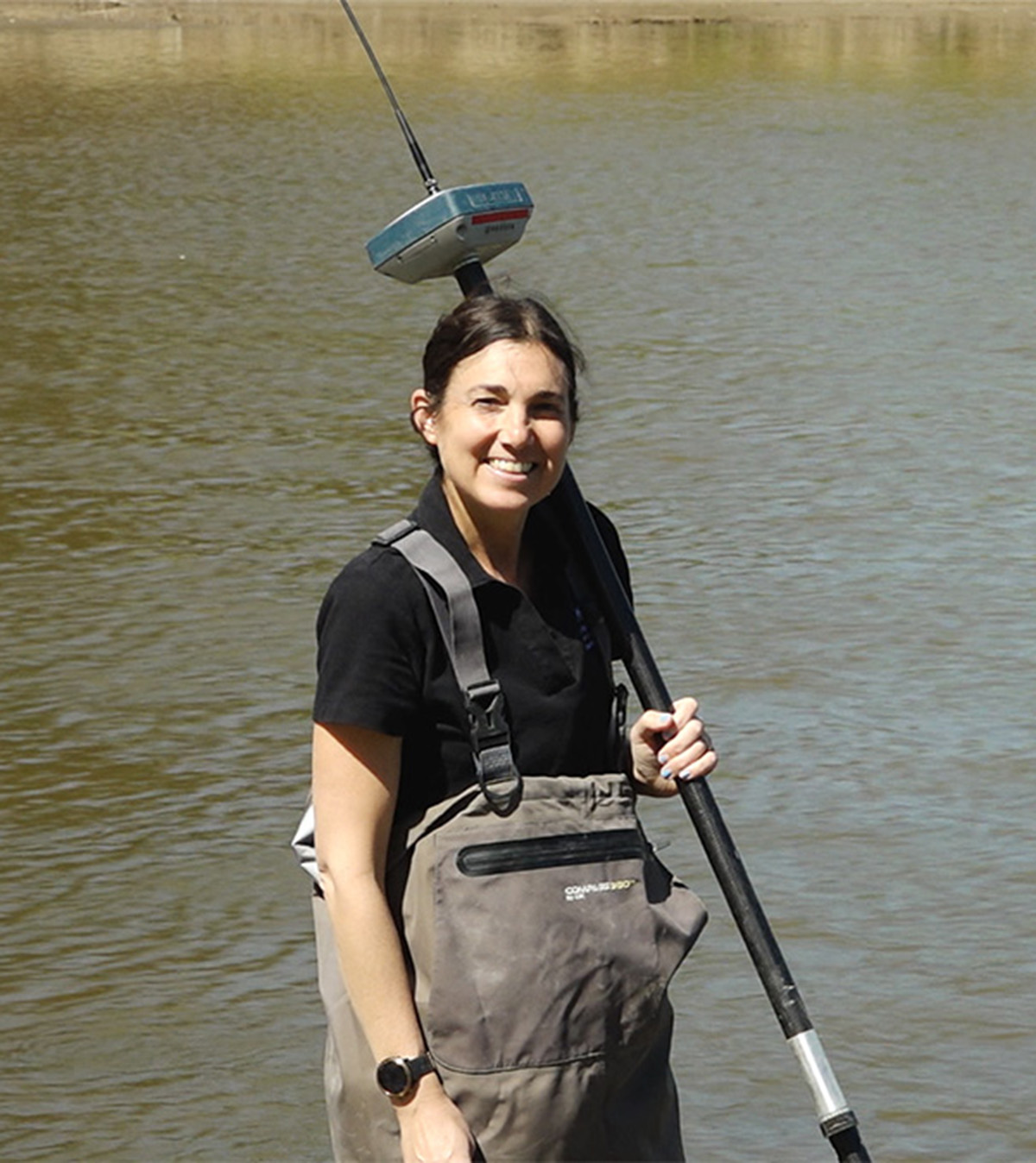 A woman smiles and holds a measuring device in front of water.
