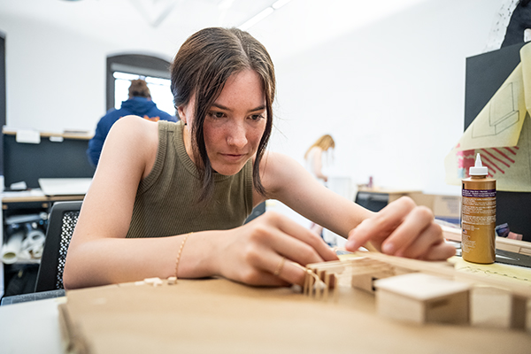 A female college student works on building a small-scale architectural model out of cardboard.