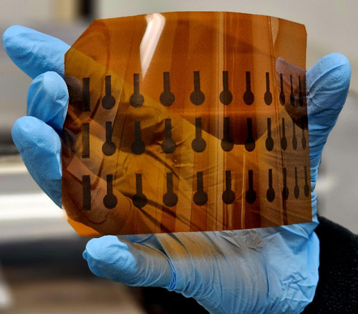A hand with blue golves holds a flexible transparent orange sheet with printed graphene phosphate sensors