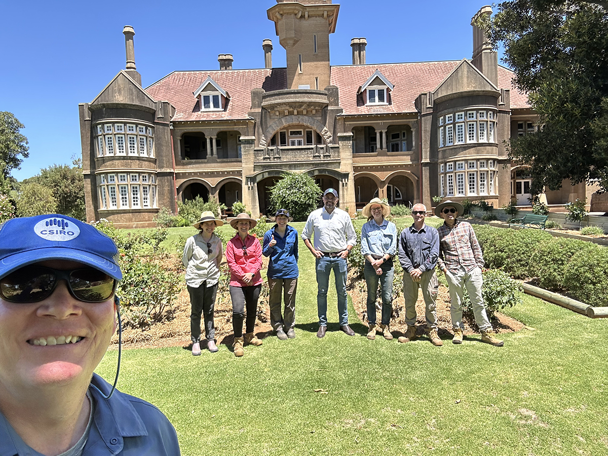 A group of researchers pose for a group portrait in front of a historic, castle-like farmstead in Australia.