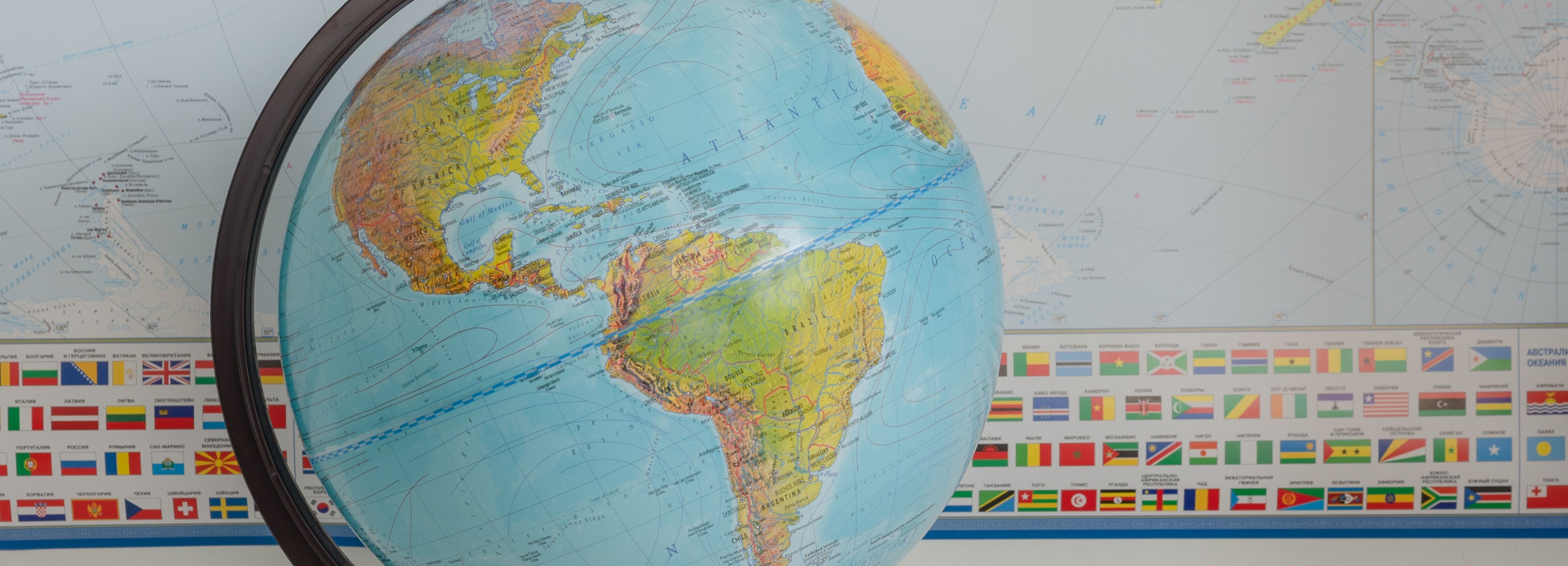 A close-up image of a globe with a map and world flags in the background