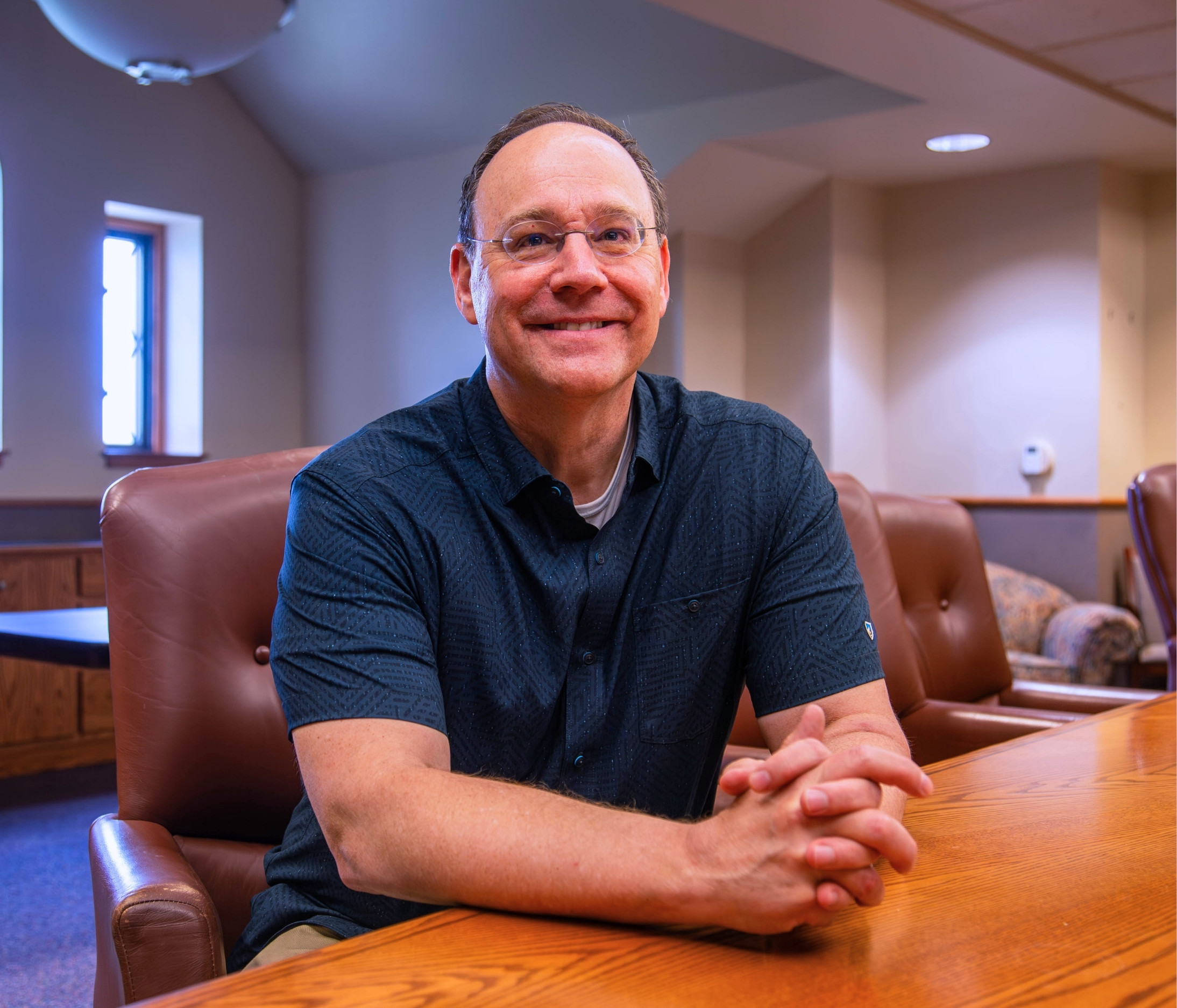 Jeff Pickering sits at a large wooden guest and smiles for a portrait.