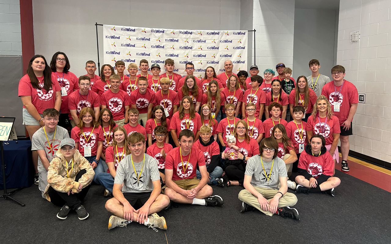 A large group of grade-school students at an engineering event all wear red branded t-shirts and smile for a group photo.