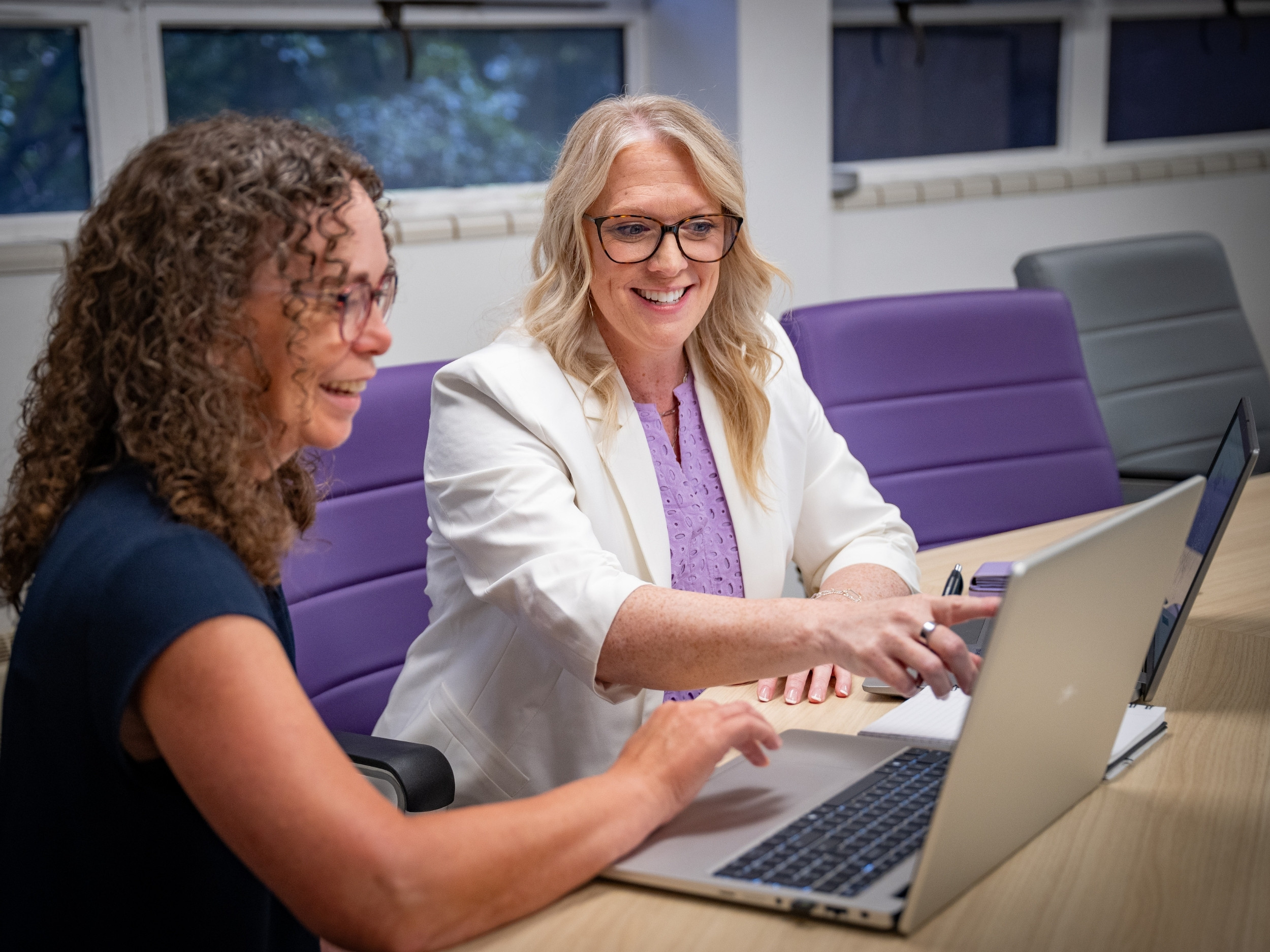 Mariah Welton-Crouser sits at a table and points at a colleague's computer