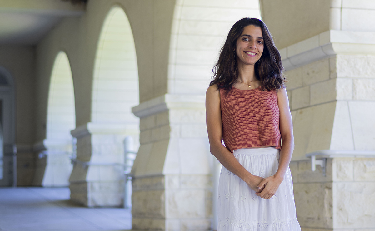 A female graduate students pose for a portrait under a library's outdoor entrance. 