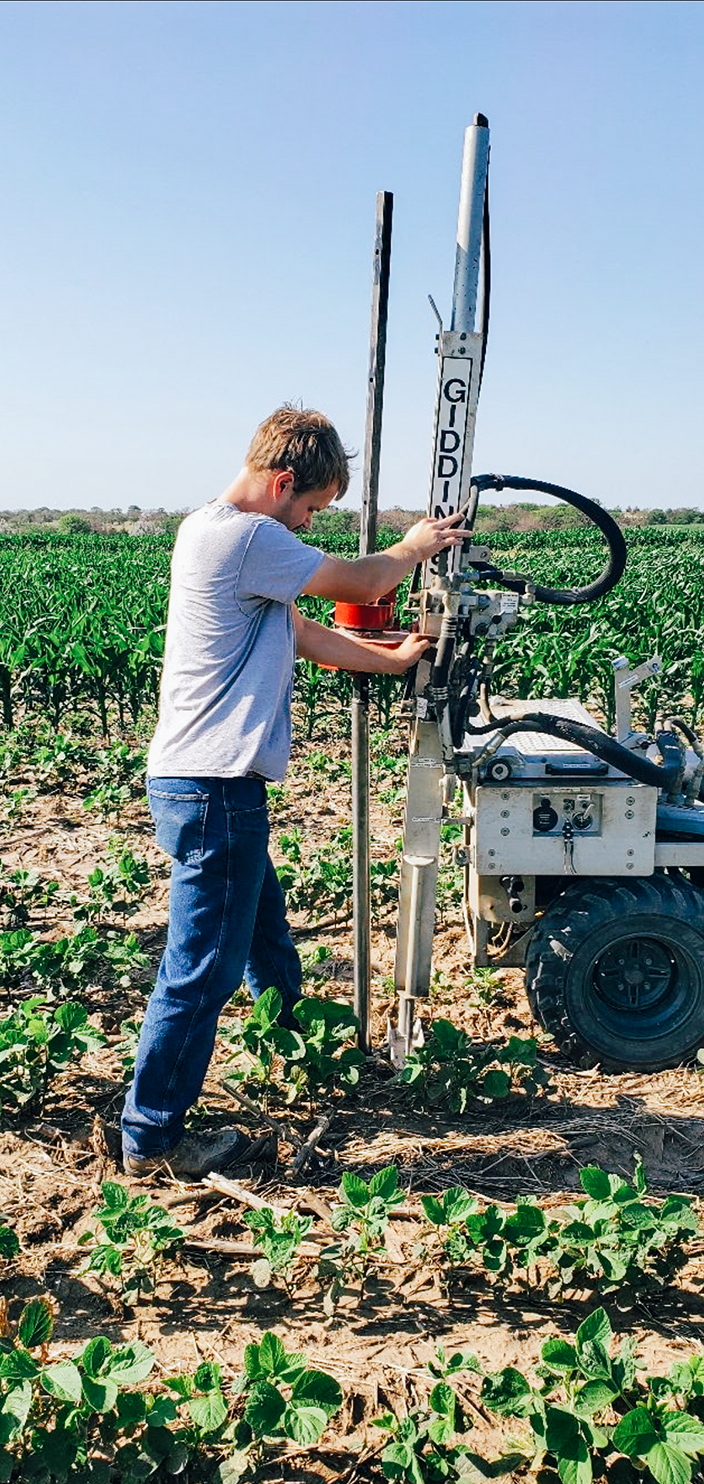 A man works in a field of green plants with equipment, including a vertical pole system