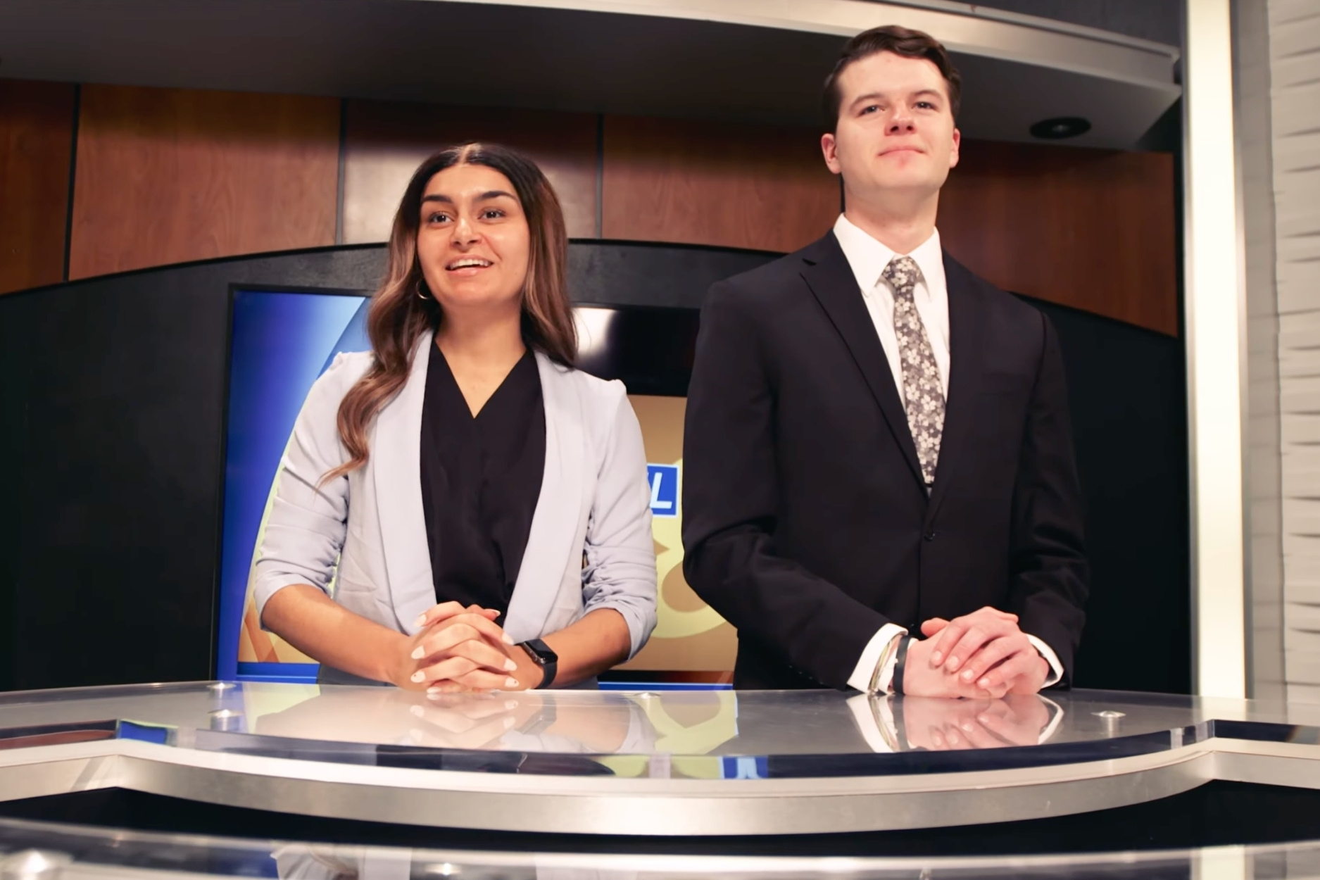 Two students stand behind a reporting desk on the set of Channel 8 news, K-State's student-run broadcast.