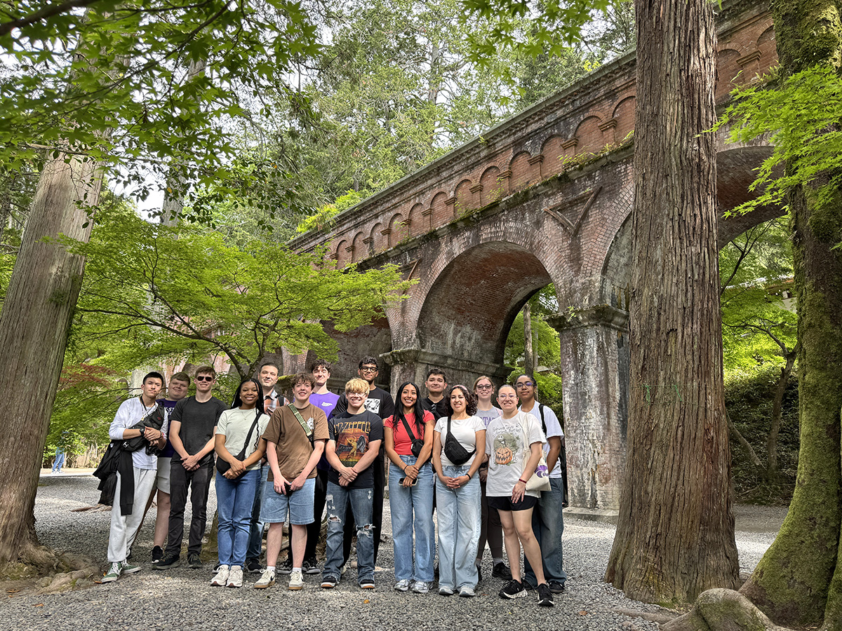 A group of student stands in front of a large aqueduct with trees surrounding them.