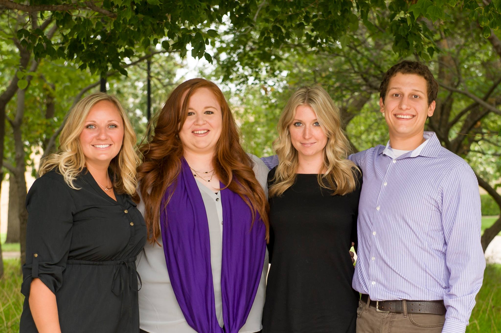 Four college graduate students pose for a professional portrait outside.