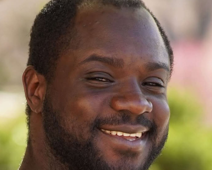 Student smiles for a portrait in front of a green background 