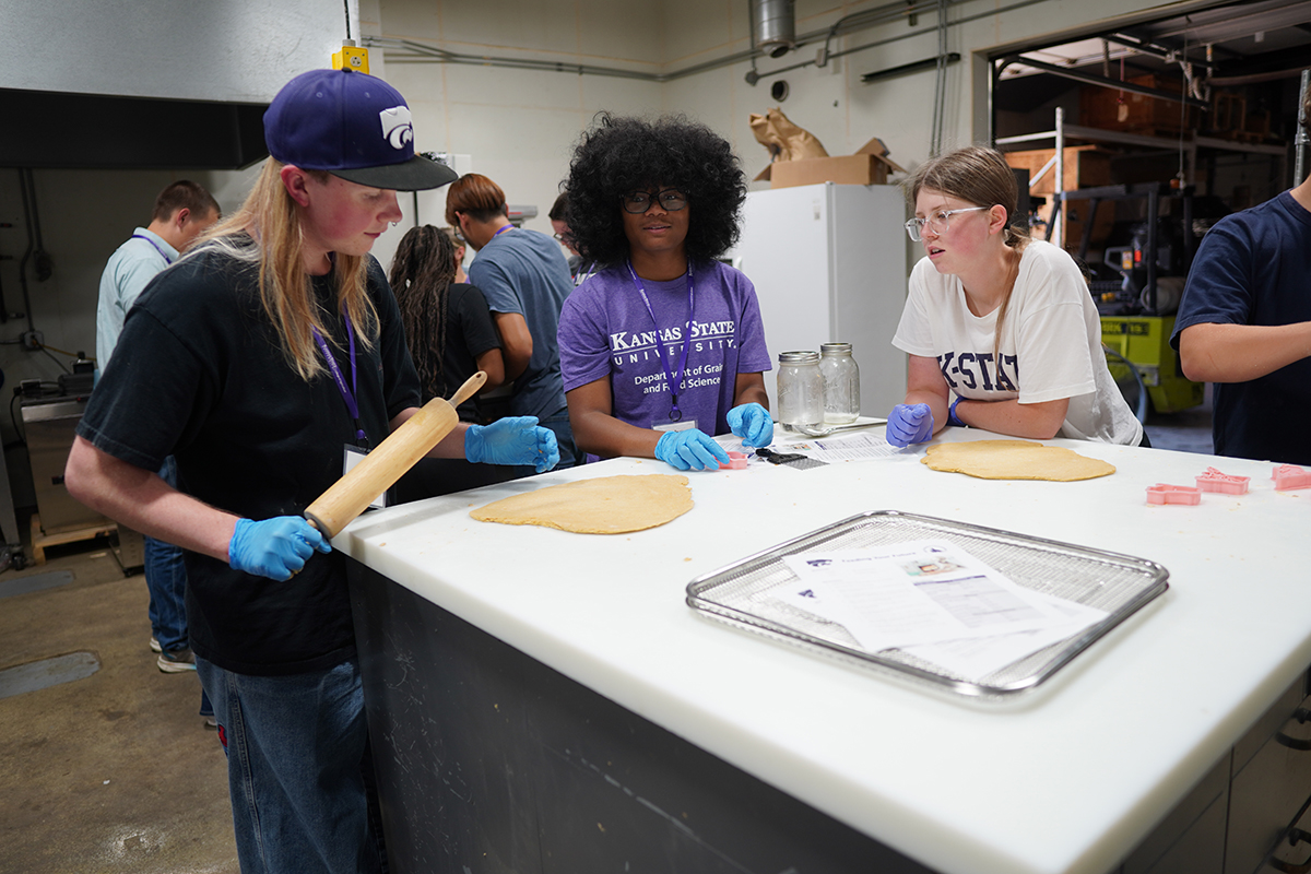 A group of high school summer camp students roll out dough in a college's baking facility.
