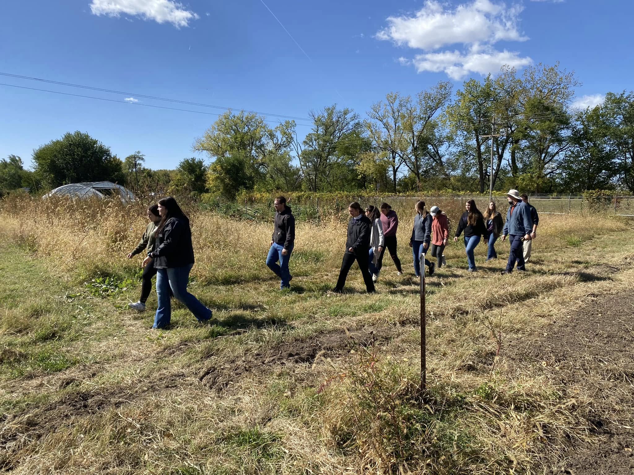 A group of college students and a professor walk through a farm on a sunny day.