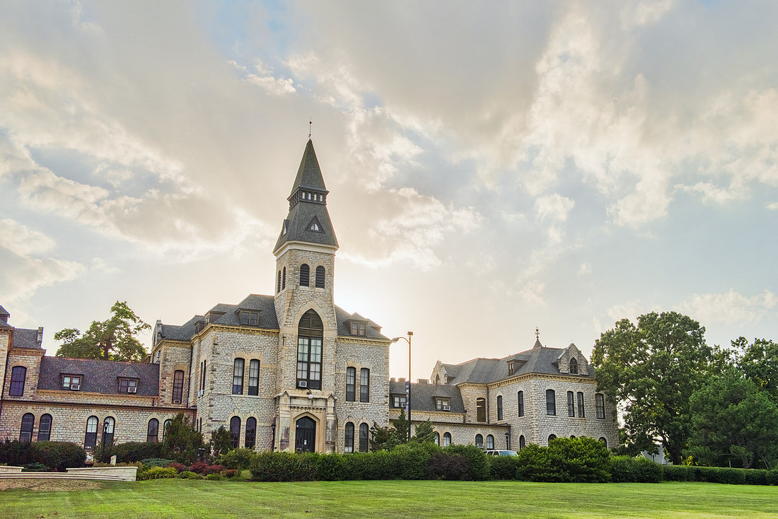 An outdoor exterior shot shows Kansas State University's Anderson Hall and its limestone tower standing tall in front of a setting sun.
