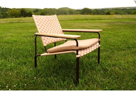 An artisticly designed chair sits on a green lawn.
