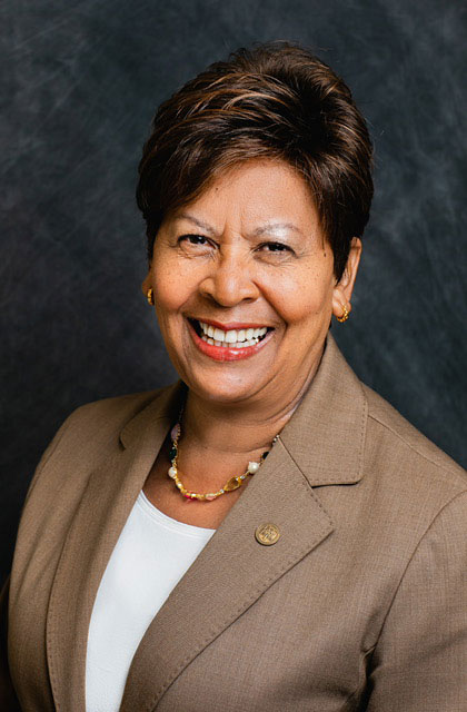 A woman in a tan jacket smiles for a portrait
