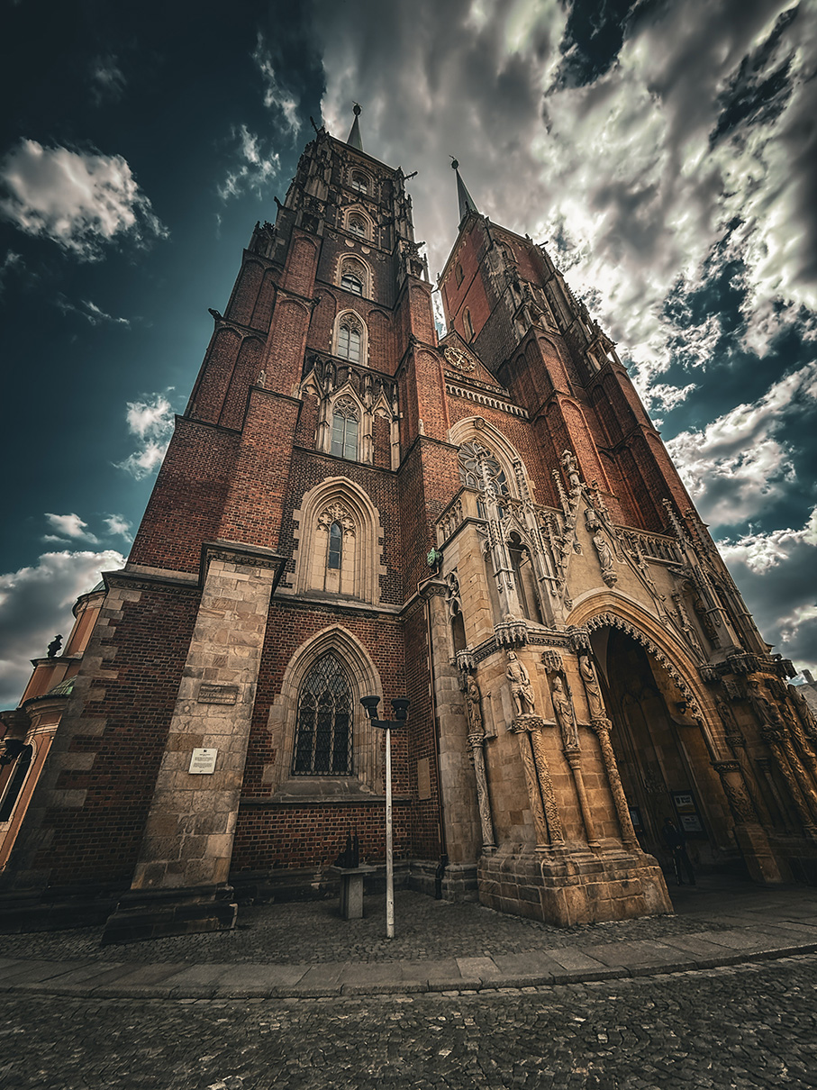 A large brick cathedral is pictured in an upward angle with a sky full of clouds above it