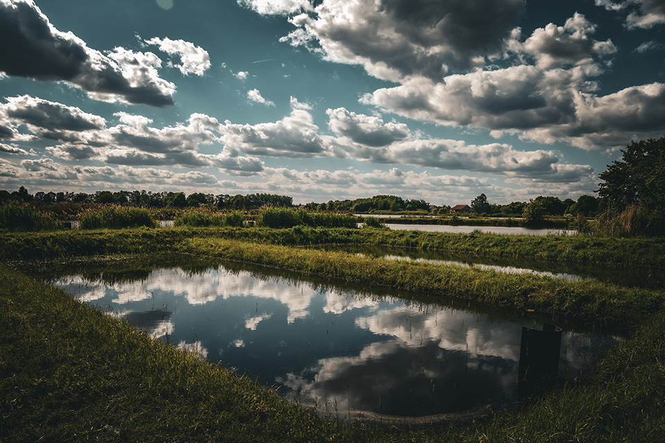 A rural landscape with small pond-like water areas that reflect the blue sky and cloud
