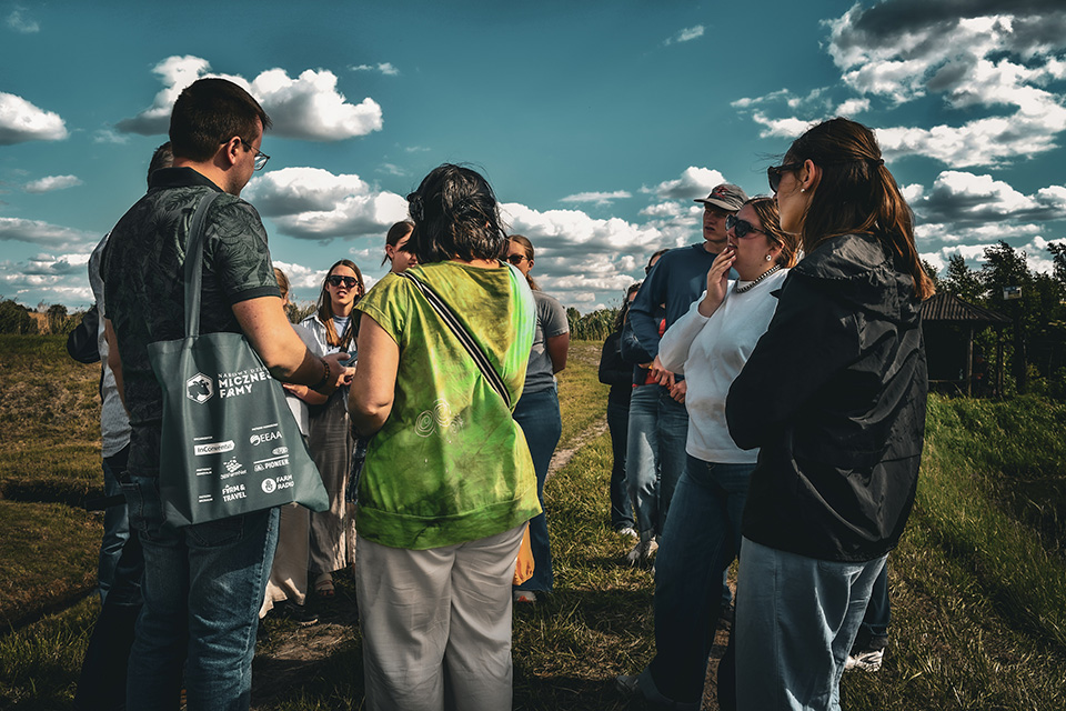 A group of students circles up in a field in Poland with a blue sky full of clouds overhead