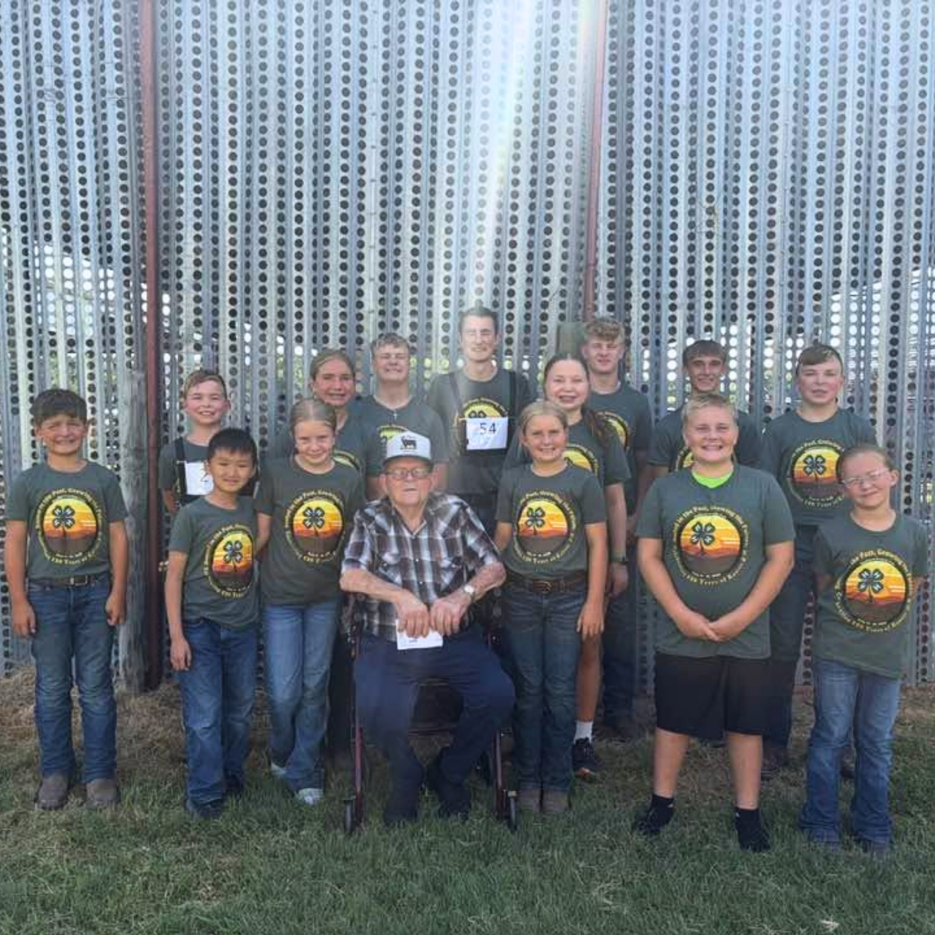 Marion Alpers sits surrounded by 14 of his great-grandchildren, all wearing 4-H shirts.