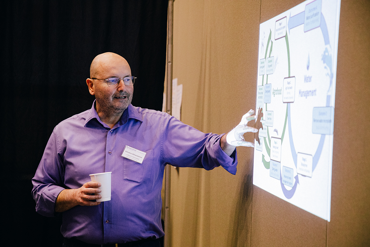 A male professor stands and points to a diagram projected onto a wooden wall.