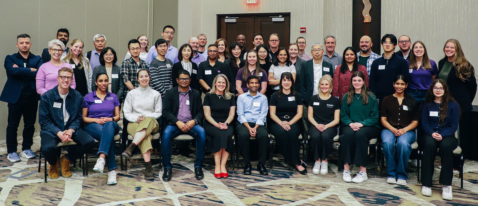 A group of about 50 college faculty, staff, judges and students sit in a large semicircle and pose for a group portrait.