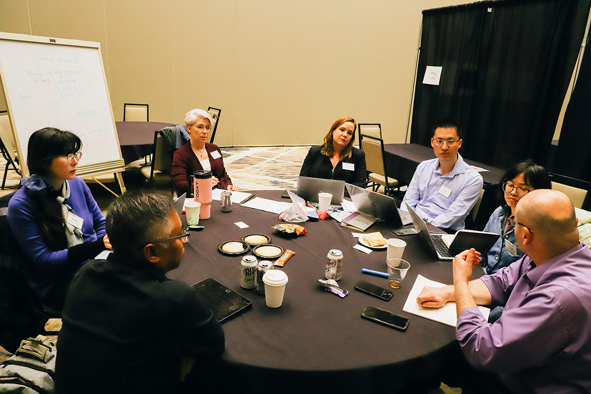 A group of college faculty hold a discussion at a circular conference table.
