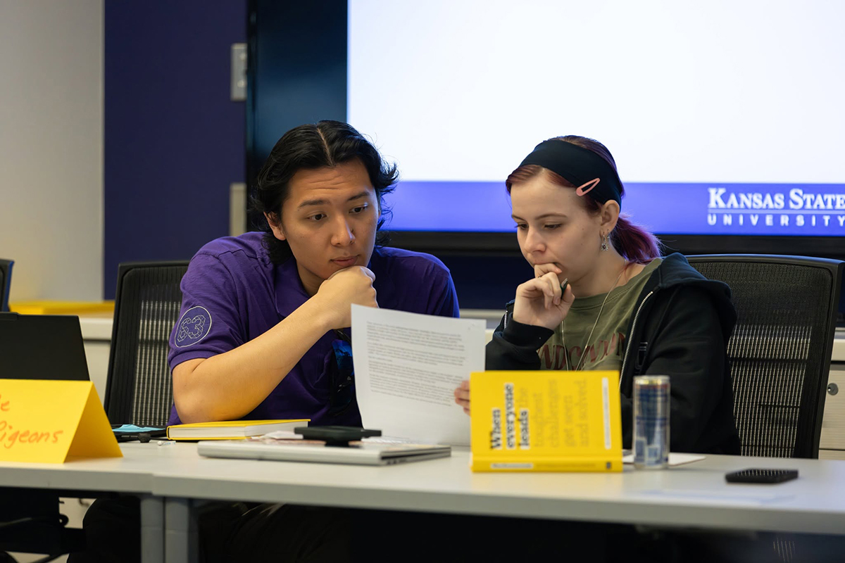 Two college students sit at a wooden table and hold a discussion.