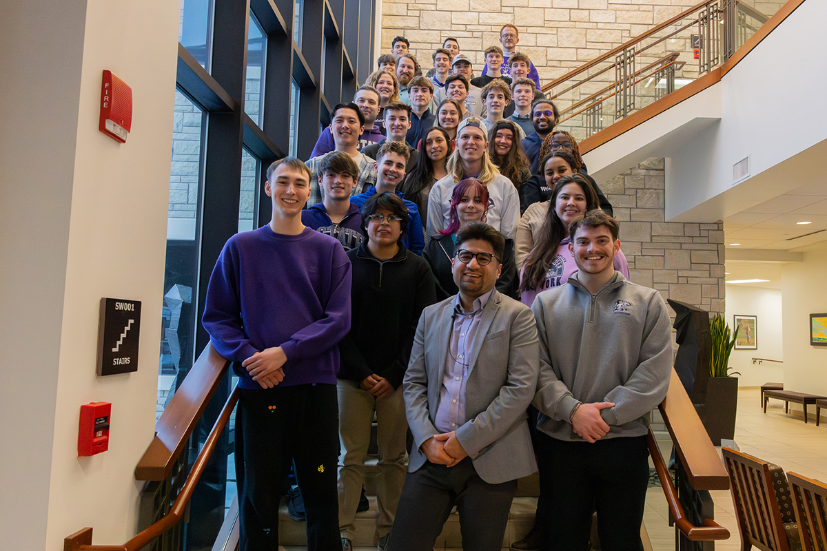A group of people stand for a portrait on a college hall's stairway.