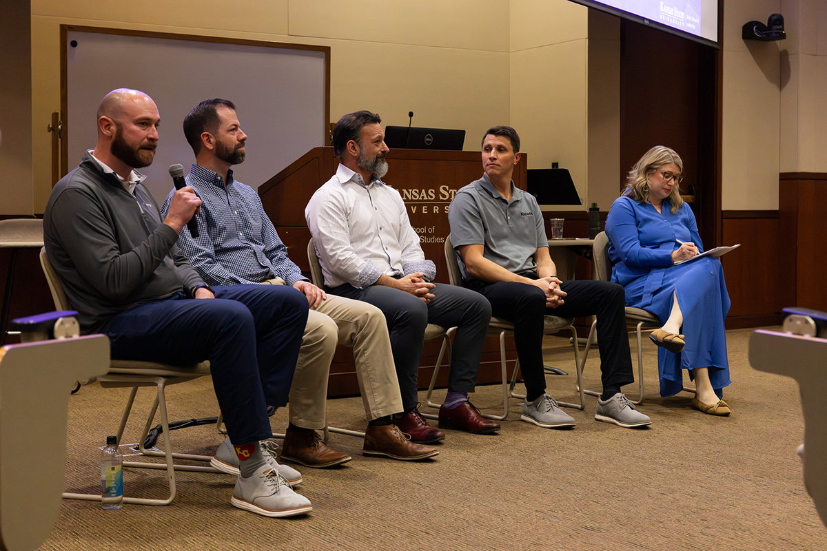 A group of adults sit on chairs at the front of a large classroom as part of a discussion panel.