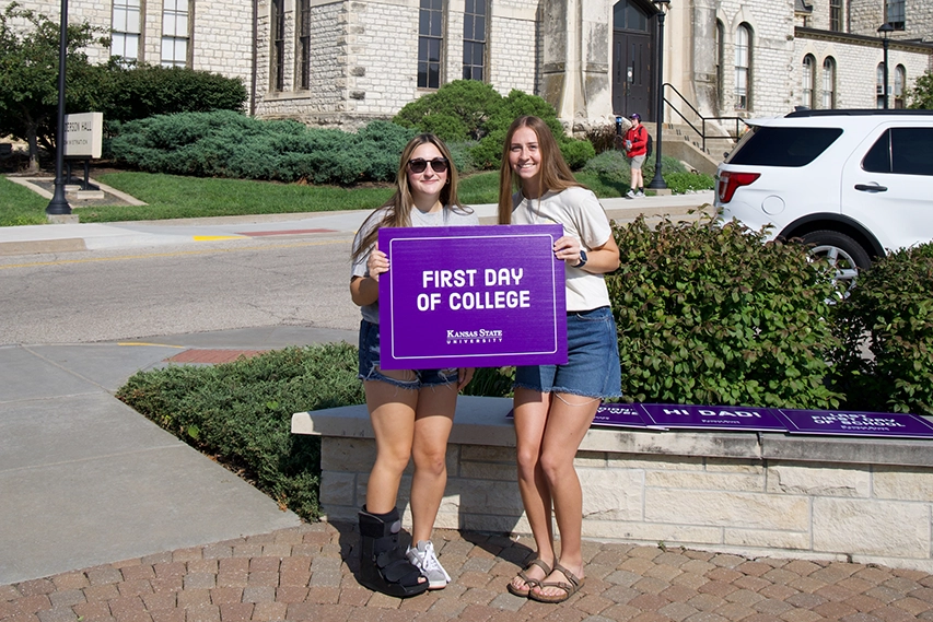 Two girls standing in front of Anderson Hall with a sign that says “First Day of College.