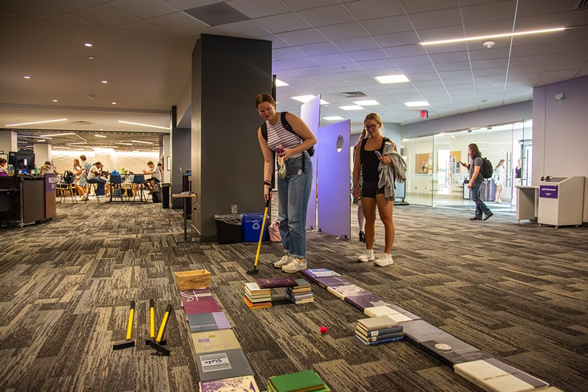 A student hitting a golf ball through stacks of books.