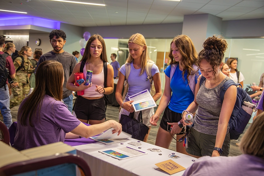 A group of students standing around an information table.