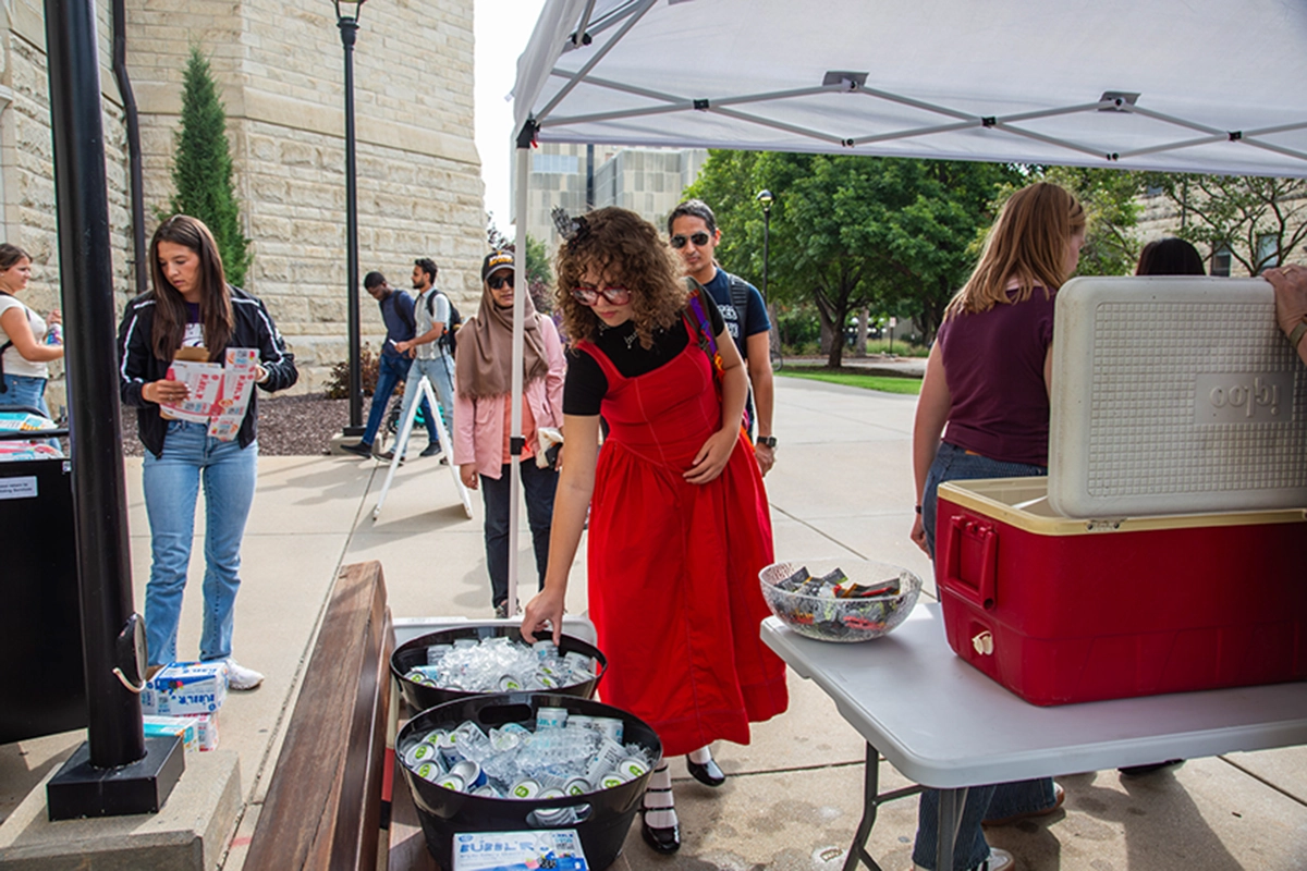 A woman in a red dress grabs a drink out of a cooler with ice in a tent outside of Hale Library.