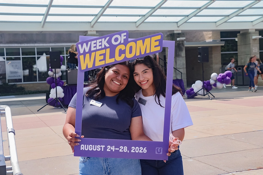 Two girls standing in front of Anderson Hall with a sign that says “First Day of College.”