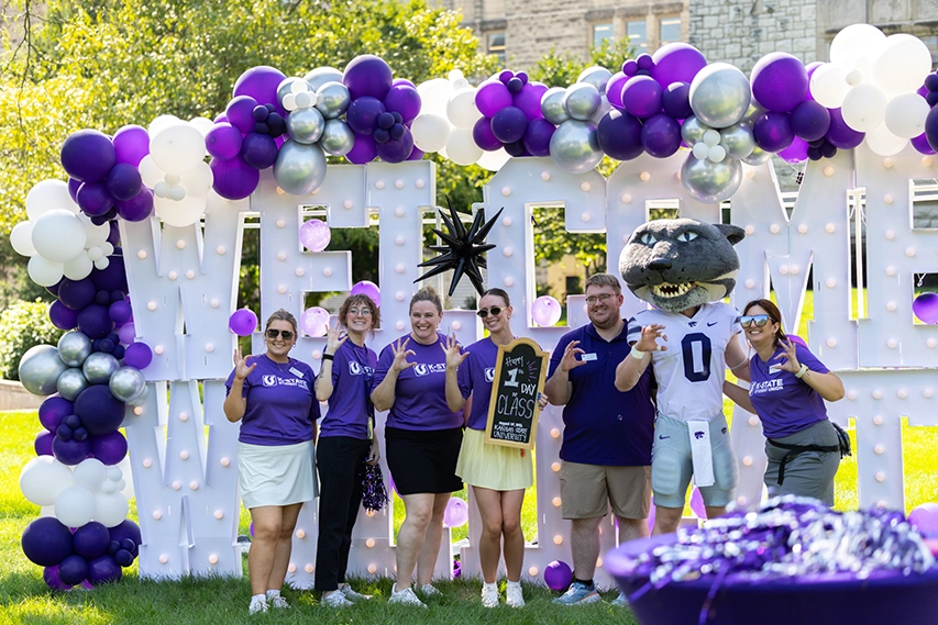 A group of staff members taking a group photo with Willie the Wildcat in front of giant letters that spell out “Welcome Wildcat."