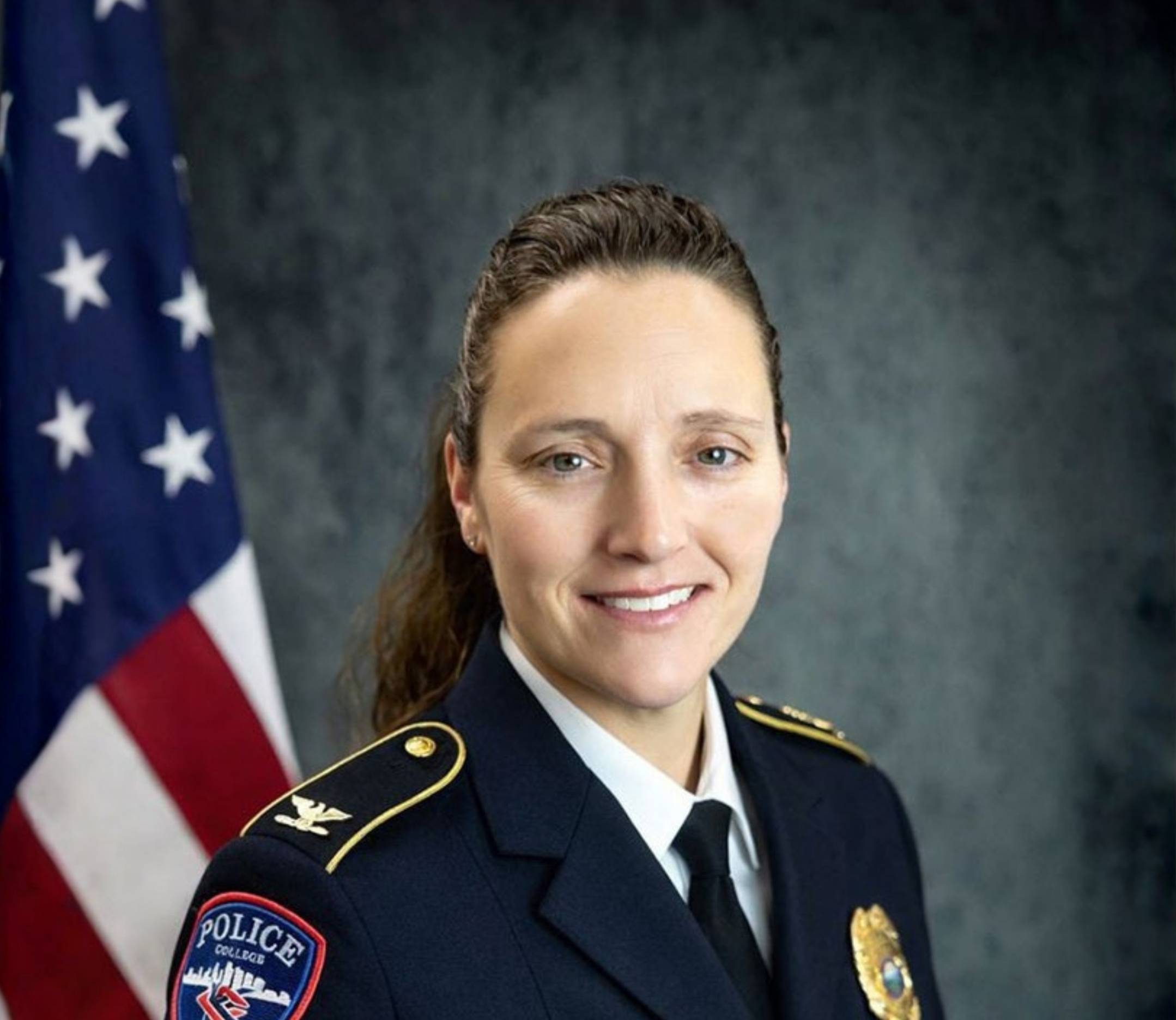 Portrait of a woman with dark hair in a police uniform with an American flag in the background