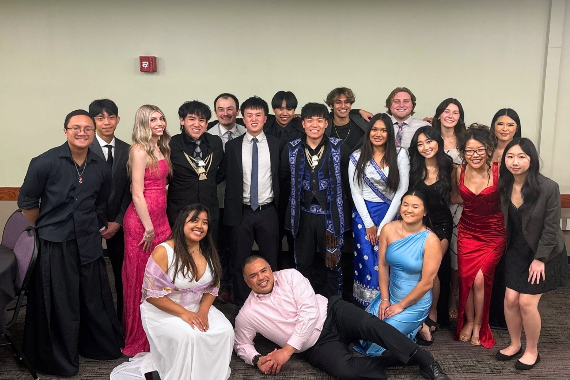 Kevin Santos Flores lays at the front of a group picture with 18 students behind him.